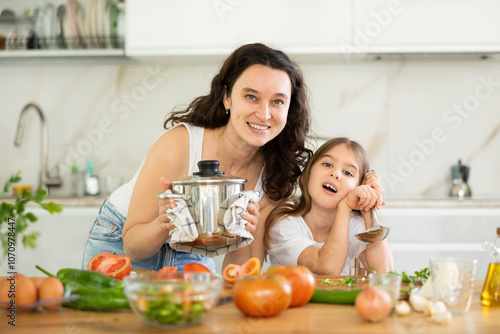 Obraz na plátně Mom and little daughter are standing at kitchen table with dishes in their hands