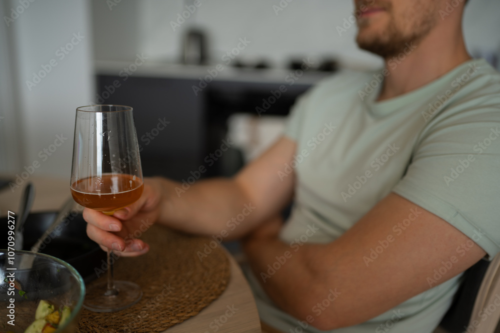 A young man enjoying a refreshing beverage in a glass, seated comfortably in a modern kitchen or dining area. He appears relaxed, sipping from a wine or cocktail glass, giving a casual vibe. A young man enjoying a refreshing beverage in a glass, seated comfortably in a modern kitchen or dining area. He appears relaxed, sipping from a wine or cocktail glass, giving a casual vibe.