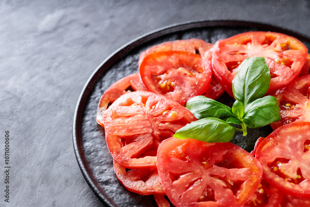 Juicy Tomato Slices with Fresh Basil Leaves on Black Plate, Dark Grey Textured Background, Top View, Copy Space Juicy Tomato Slices with Fresh Basil Leaves on Black Plate, Dark Grey Textured Background, Top View, Copy Space