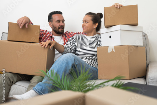 New Beginnings: A contented married couple takes a breather on the sofa, amidst a sea of cardboard boxes, embracing exhaustion and happiness as they settle into their new home photo