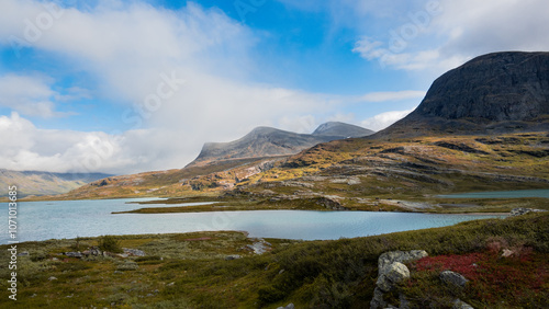 Beautiful nordic swedish landscape during autumn season with blue sky, mountains, sunshine over grassy meadow and azure lake evokes far north, wilderness, remote and adventure when hiking Kungsleden.