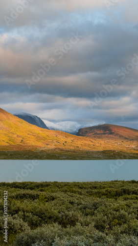 Clouds over glacier and mountains with calm lake beautifuly englighted by autumn golden light during evening in swedish nordic wilderness of Lapland evokes adventure, solitude and harsh landscape. photo