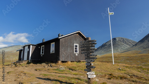 Salka mountain wooden hut with guidepost and mountains on the horizon, located on Kungsleden trail during beautiful sunny day in the wilderness of arctic Lapland. Sweden. photo