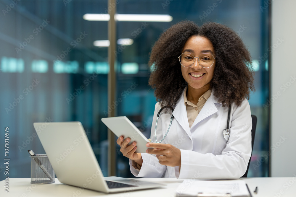 Smiling African American woman doctor using tablet in office. Wearing white coat and stethoscope, representing technology in healthcare. Promotes modern communication and patient engagement. Smiling African American woman doctor using tablet in office. Wearing white coat and stethoscope, representing technology in healthcare. Promotes modern communication and patient engagement.