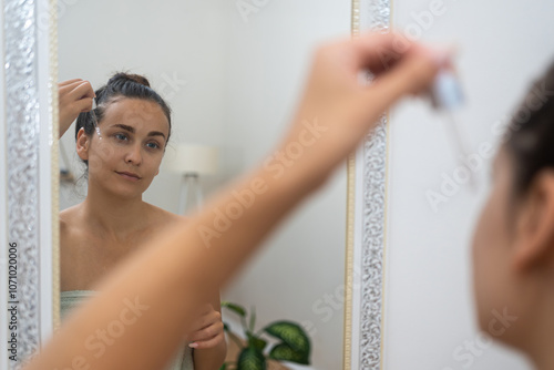 Mirror moment: A woman enhances her anti-aging skincare, using a serum dropper to apply hyaluronic acid in her home.  photo