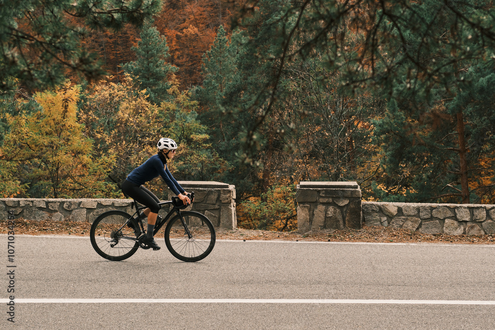 Fototapeta premium Woman cyclist rides road bike through scenic autumn landscape. Perfect for travel, sports, and healthy lifestyle themes. Romania. Carpathian Mountains. Transylvania