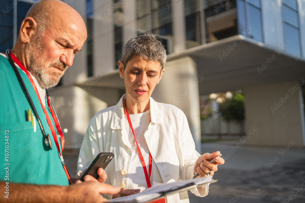 Two doctors man and woman review patients record with mobile phone Two doctors man and woman review patients record with mobile phone