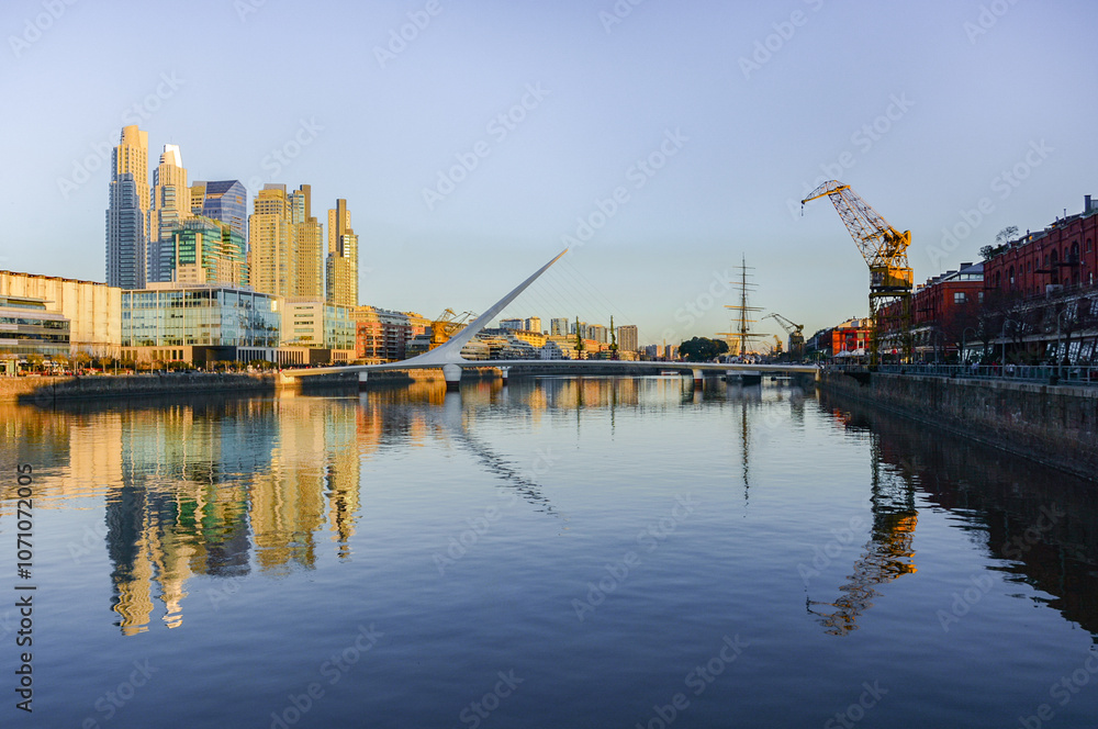 Naklejka premium Cityscape of Puerto Madero neighborhood with Puente de La Mujer or Woman's Bridge, High-rise buildings, harbour and river during sunset in Buenos Aires, Argentina. With copy space