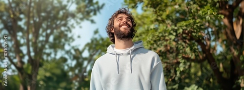 Smiling young man outdoors, enjoying nature on a sunny day, symbolizing relaxation, positivity, and well-being, with a lush, green background.