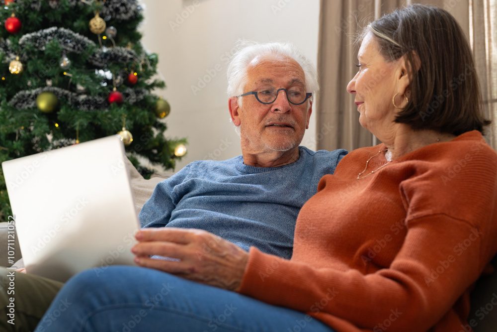 Elderly couple enjoying Christmas together at home with laptop, feeling content Elderly couple enjoying Christmas together at home with laptop, feeling content