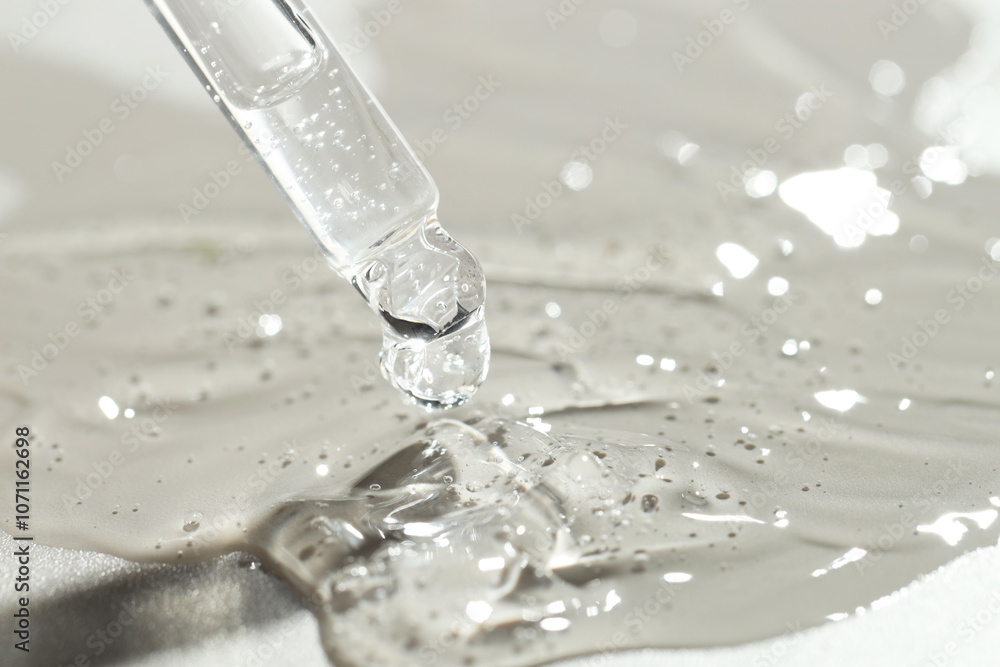 Dripping cosmetic serum from pipette on grey background, closeup Dripping cosmetic serum from pipette on grey background, closeup