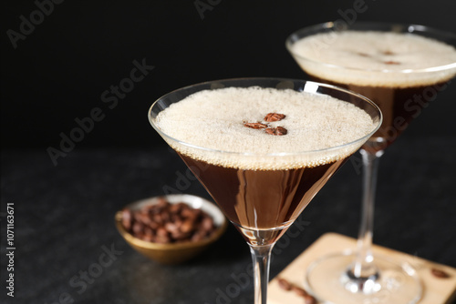 Delicious espresso martini with coffee beans in glasses on blurred black background, closeup