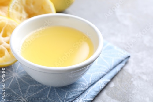 Fresh lemon juice in bowl and fruit on grey table, closeup