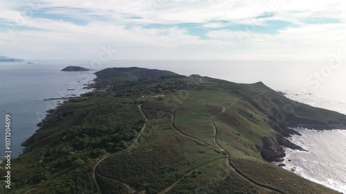 Aerial view over Ons Island, capturing its winding paths, rocky cliffs, trees, lighthouse and Barrio do Curro with harbor pier. Tranquil Atlantic Ocean and cloudy skies. Onza island in background. photo