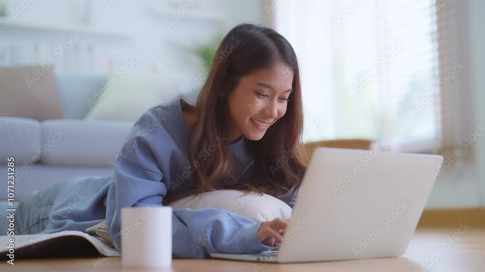 Beautiful young Asian woman with laptop lying on floor in living room. Relaxing at home Beautiful young Asian woman with laptop lying on floor in living room. Relaxing at home