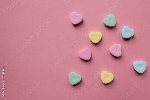 flat lay of scattered pastel colored candy hearts in pink, green, and yellow against a pink background with copy space available; valentines day themed