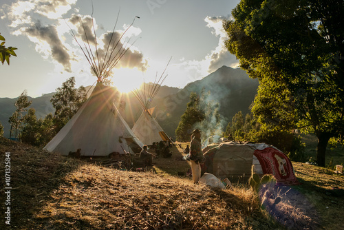 Native community with people in a landscape with teepee and temazcal in a sunrise with the sun rising over the mountains.  photo