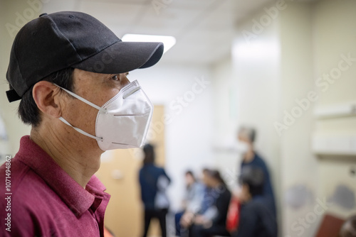Man wearing a facemask at the hospital waiting room.  Unrecognizable people in a corridor in the hospital.