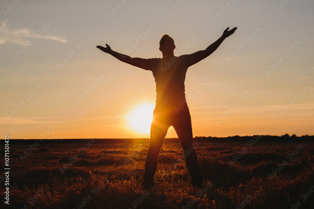 Fototapeta premium Man with Arms Outstretched in Field at Sunset