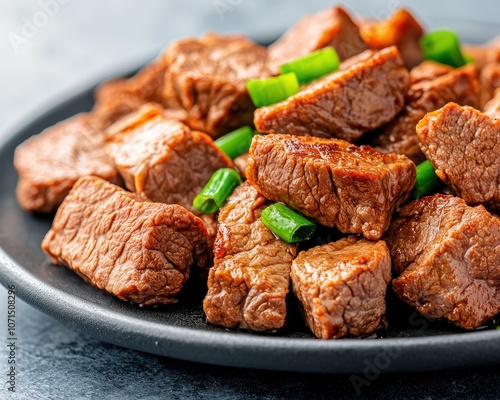 Close-up of stir-fried beef cubes with green onions on a black plate. photo