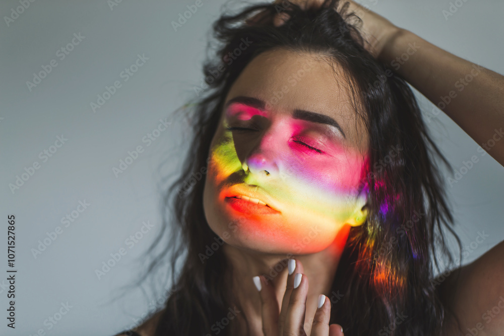 Portrait of brunette girl with rainbow on her face. Multicolored light in studio. LGBT symbol transgender transition Portrait of brunette girl with rainbow on her face. Multicolored light in studio. LGBT symbol transgender transition