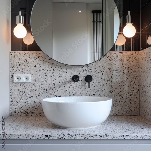 An elegant bathroom highlighting a round mirror, trendy terrazzo tiles, and a contemporary basin alongside modern lighting fixtures photo