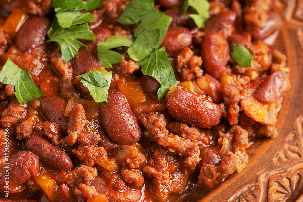 Close up view of traditional mexican spicy homemade chili con carne stew made of kidney or pinto beans, fried ground beef, tomatoes and chilli pepper served on plate decorated with fresh green parsley Close up view of traditional mexican spicy homemade chili con carne stew made of kidney or pinto beans, fried ground beef, tomatoes and chilli pepper served on plate decorated with fresh green parsley