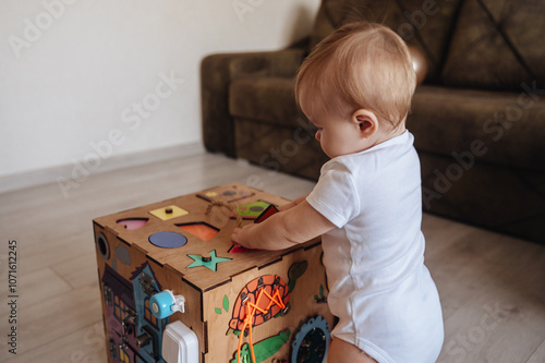 Happy toddler baby boy is playing with a busyboard cube on the nursery floor. A child aged one year photo