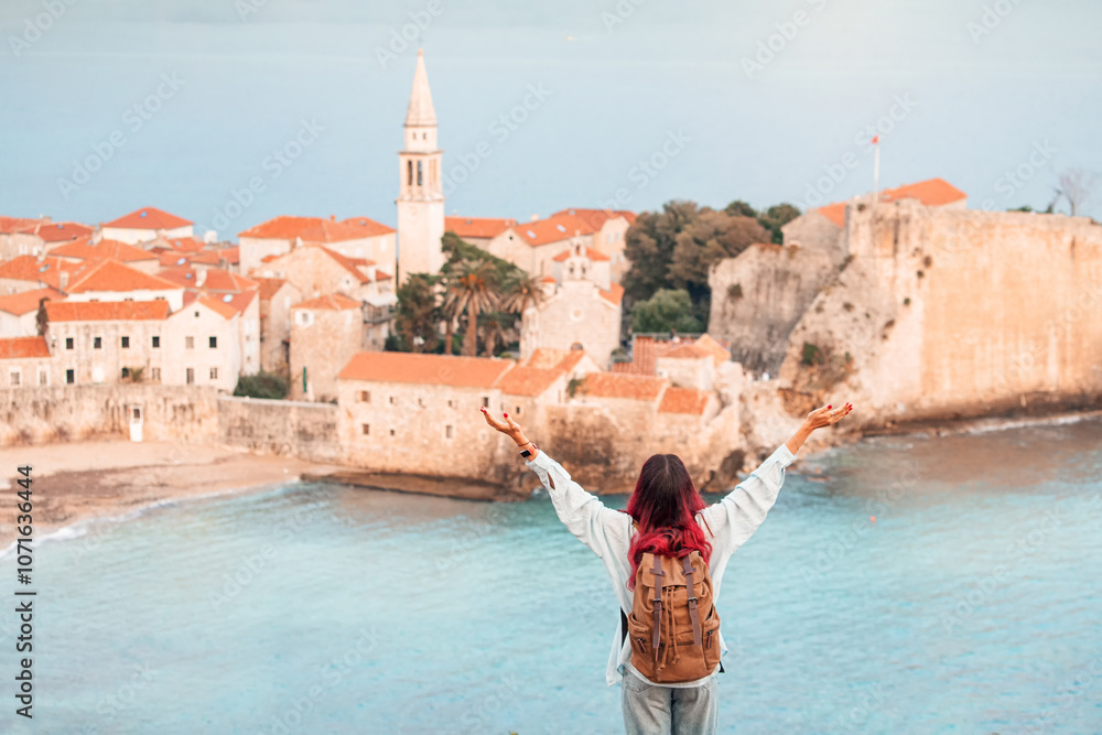 A carefree woman backpacker enjoying her summer journey, exploring famous landmarks in a European coastal city Budva, Montenegro, capturing the freedom and beauty of travel