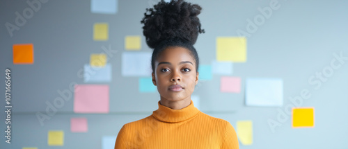 Portrait of a woman in a bright sweater, standing in front of a wall with colorful sticky notes, showcasing creativity and focus.