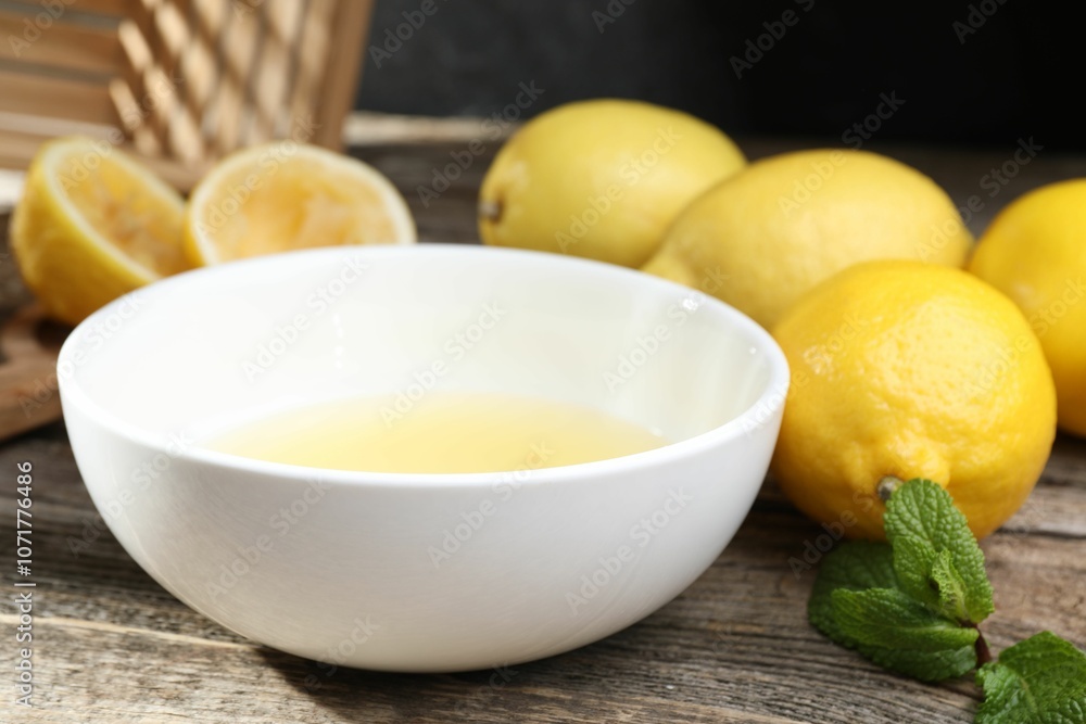 Fresh lemon juice in bowl and fruits on wooden table, closeup Fresh lemon juice in bowl and fruits on wooden table, closeup