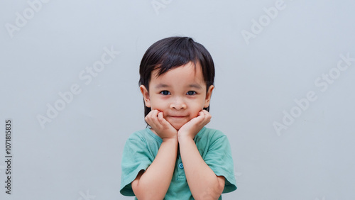 Studio portrait of a adorable little boy holding his cheeks with his hands on a grey background