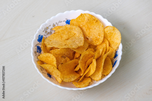Obraz na plátně A bowl of crispy potato chips on light wooden Surface