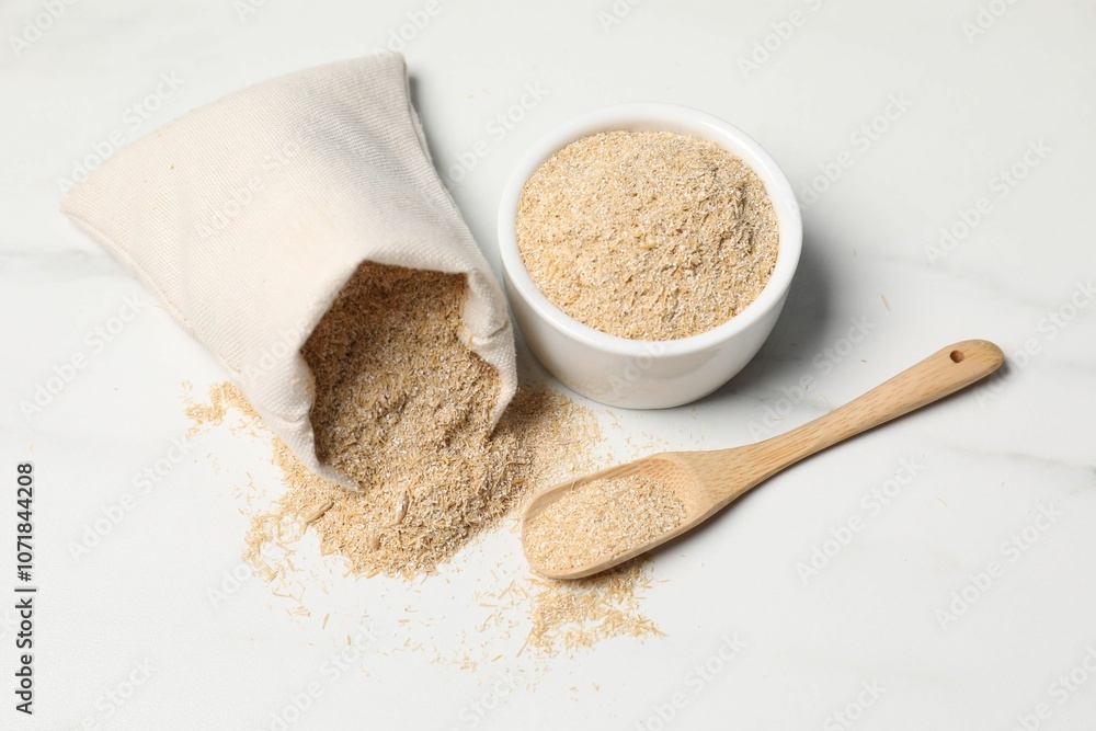 Oat bran in burlap bag, bowl and wooden spoon on white marble table