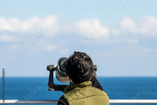 female tourist looking at the sea through a telescope photo