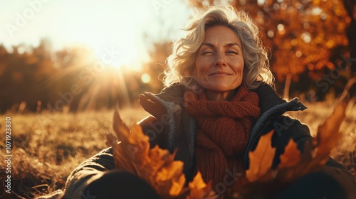 A content middle-aged woman smiles with closed eyes as sunlight streams through fall trees, embracing the warmth and tranquility of the autumn ambiance. photo