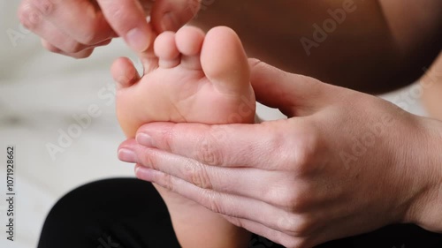 The mother is doing massage of foot for child. Counting and touching the toes. Mom stroking and tickling the kid. Gentle tactile contact. Love atmosphere. Happy moments of motherhood and childhood.