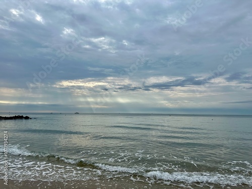 Peaceful seascape at dawn with soft waves and a distant boat under a dramatic, cloudy sky on Palavas-les-Flots beach, Mediterranean Sea, France