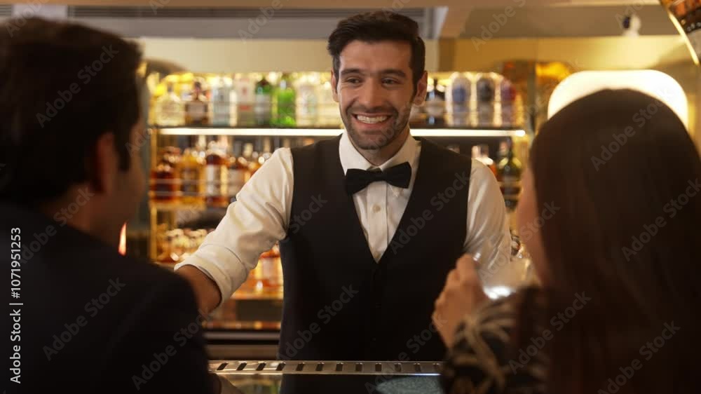 Focusing smiling smart bartender serving gin fizz or tonic soda at luxurious bar, engaging lively conversation with VIP customer couple at back view in atmosphere at lighting warm nightclub. Vinosity. Focusing smiling smart bartender serving gin fizz or tonic soda at luxurious bar, engaging lively conversation with VIP customer couple at back view in atmosphere at lighting warm nightclub. Vinosity.
