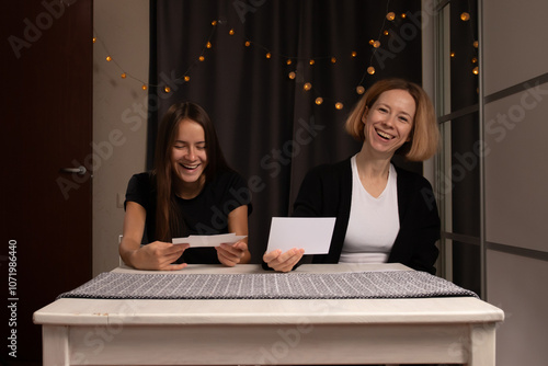 Mother and daughter looking at photos, sentimental women smiling, holding pictures together