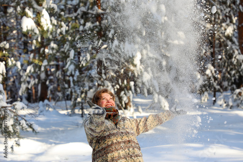 On Christmas, a woman in a snowy winter forest throws freshly fallen snow into the air and laughs joyfully.