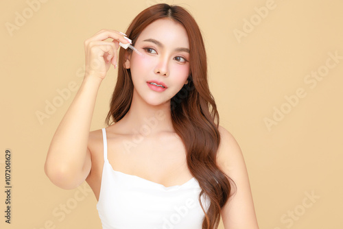 Beautiful young Asian woman model long hair using dropper for apply serum on face clean fresh skin on isolated beige background. Cute girl portrait, Facial treatment, Body care, Beauty and Spa.