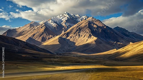 Majestic mountain range with sunlit peaks and grassy valleys under a dramatic sky. Scenic landscape for travel and nature
