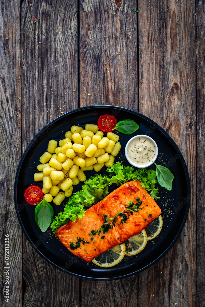 Seared salmon steak with gnocchi and lemon slices served on black plate on wooden table. Top view
Seared salmon steak with gnocchi and lemon slices served on black plate on wooden table. Top view