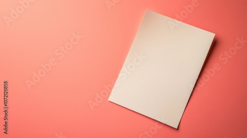 A blank sheet of paper rests on a coral background, conveying minimalism and simplicity in design. photo