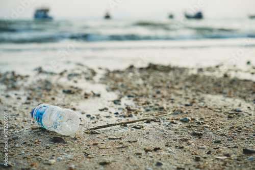 Plastic pet bottle left on the sandy beach, waste pollution or garbage on the blur beach background. Rubbish disposal and trash management, Environmental pollution concept. photo