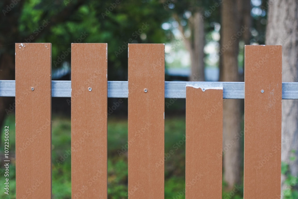 section of a fence made up of vertical brown wooden slats attached to horizontal metal bars.The wooden slats are evenly spaced and secured to the metal bars with screws. section of a fence made up of vertical brown wooden slats attached to horizontal metal bars.The wooden slats are evenly spaced and secured to the metal bars with screws.