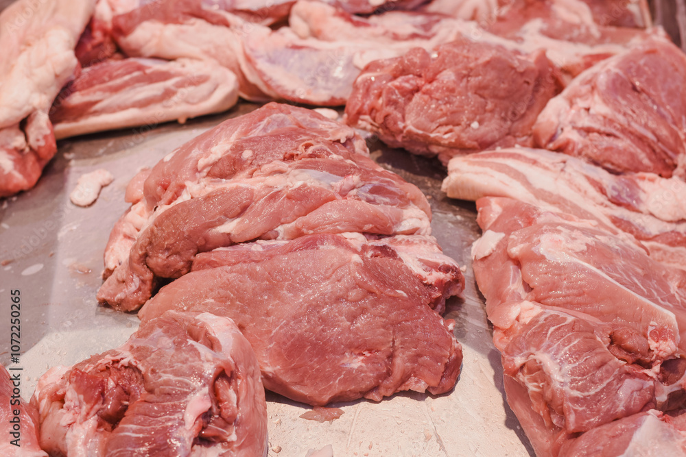several pieces of raw pork meat placed on a metallic surface. The meat appears fresh, with visible marbling of fat and muscle tissue. The pieces vary in size and shape. several pieces of raw pork meat placed on a metallic surface. The meat appears fresh, with visible marbling of fat and muscle tissue. The pieces vary in size and shape.