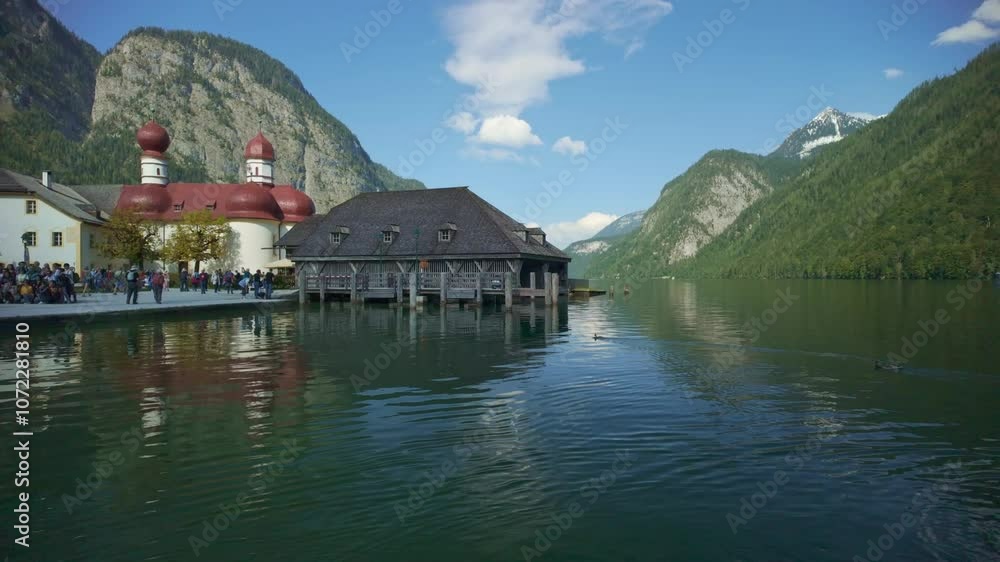 A bright day with many tourists at St Bartholoma with view of Konigsee natural lake at Berchtesgaden in Bavaria Germany with beautiful Church serene water in foreground Bavarian alps in the background A bright day with many tourists at St Bartholoma with view of Konigsee natural lake at Berchtesgaden in Bavaria Germany with beautiful Church serene water in foreground Bavarian alps in the background