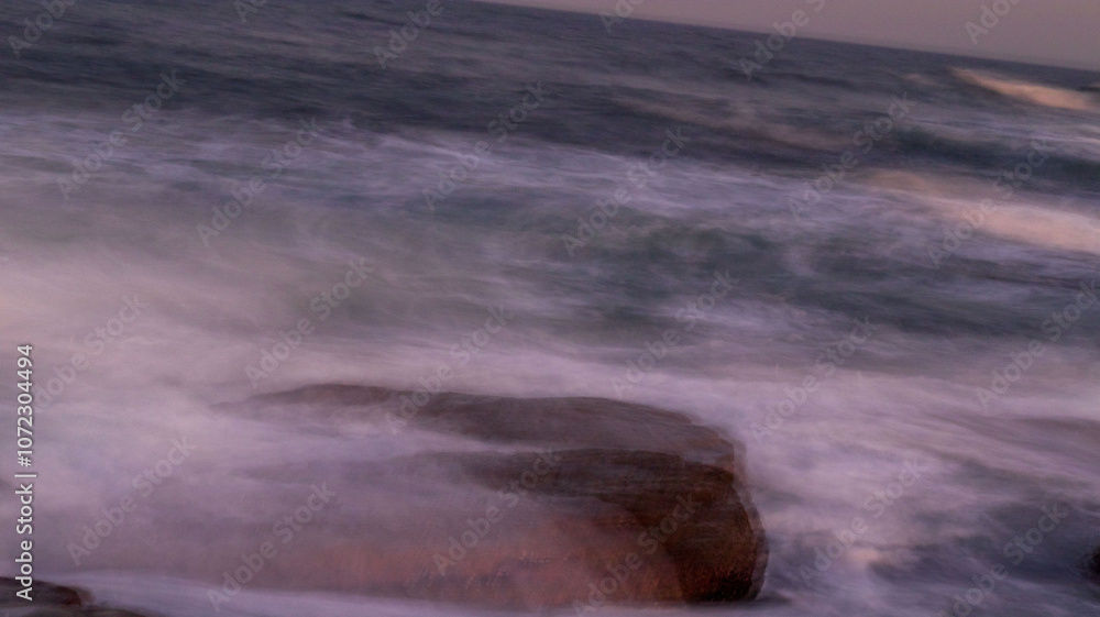 Slow shutter speed photo of ocean water flowing over a rock, located at orange rocks in Margate South Africa